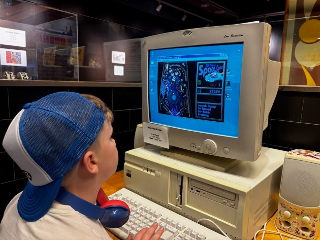 a child with his hat backward playing Space Cadet 3D Pinball on a PC with a floppy diskette drive.